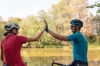 Nehir kıyısında iki bisikletçi beşlik çakıyor.