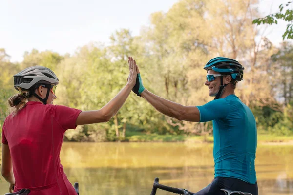 Two cyclists high-five each other on a river shoreline