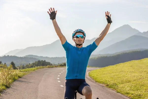Ciclista masculino montando uma bicicleta com os braços levantados, em uma pose de vitória — Fotografia de Stock