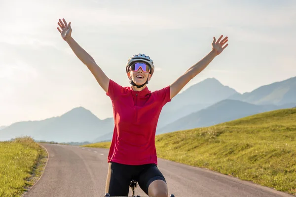 Feminino ciclista de corrida levantando braços em uma pose de vitória, tiro largo — Fotografia de Stock