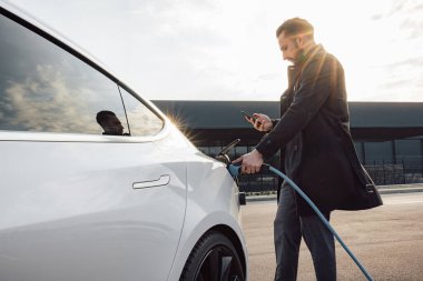 Zarif bir işadamı, gün batımında ticaret merkezinin otoparkında yeni bir elektrikli araba şarj ediyor.
