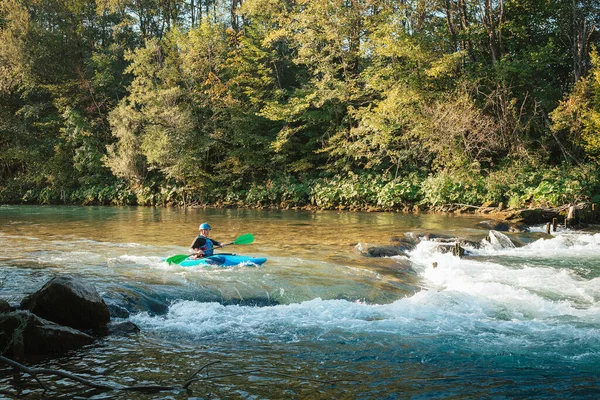 Male recreational athlete paddling carefully over the risky, foamy, and splashy whitewater rapids in his blue kayak