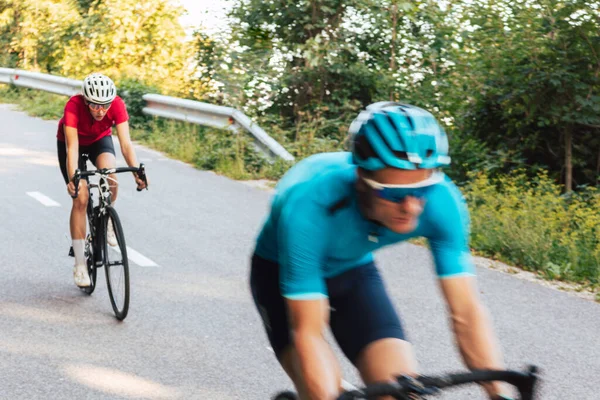 Profesyonel yarış bisikletleri üzerinde iki motosikletlinin ormandaki virajlı yolda hızla yokuş aşağı gitmesinin bulanık hareketi.