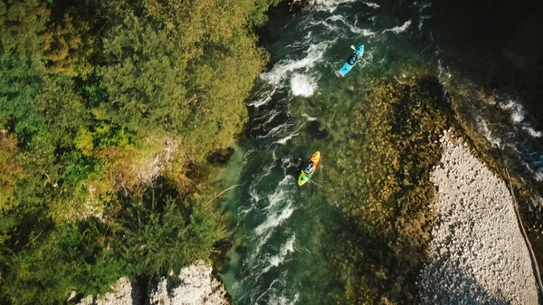 Two recreational athletes kayaking over fast moving water, paddling and successfully maneuvering between river rock obstacles, aerial drone view.
