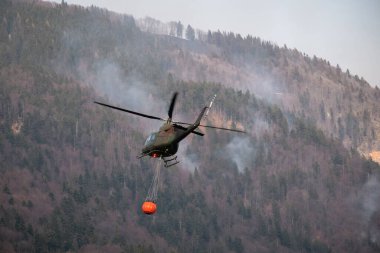 Ormanda yangın var, helikopterle su kovası taşıyor.