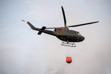 Wildfire firefighting in forest with helicopter carrying a water bucket