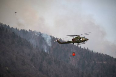 Ormanda yangın var, helikopterle su kovası taşıyor.