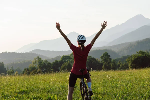 Happy female road racing cyclist in joy, with arms raised above her head, after successfully reaching a goal