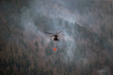 The helicopter carrying a bucket to deliver water for aerial firefighting in a mountain forest