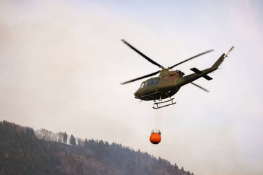 Localized wildfire with the helicopter dropping water by using a water bucket attached to a long line under the helicopter