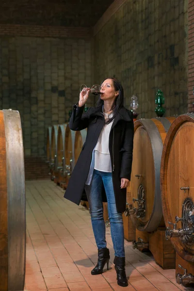 Woman tasting wine at the wine cellar with barrels in background