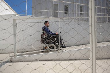 Man on electric wheelchair moving along concrete accessibility pathway near the building. Concept of wheelchair access facilitates.