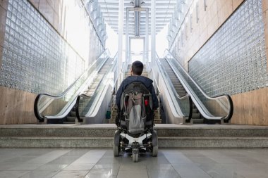 Person with disability on electric wheelchair stopping at the bottom of inaccessible staircase, unable to reach the top