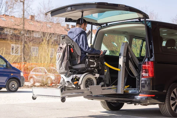 Man with disability using hydraulic wheelchair lift to get in the van, after a summer day spent on beautiful mountain nature