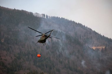 Localized wildfire with the helicopter dropping water by using a water bucket attached to a long line under the helicopter