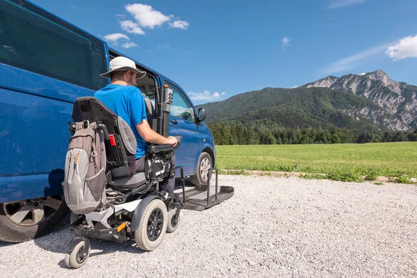 Man with disability using hydraulic wheelchair lift to get in the van, after a summer day spent on beautiful mountain nature