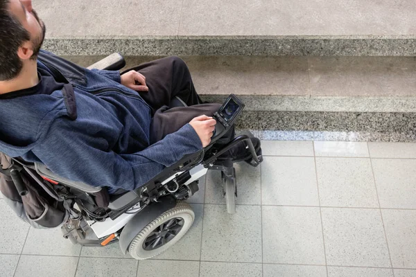 Person with disability on electric wheelchair stopping at the bottom of inaccessible staircase, unable to reach the top