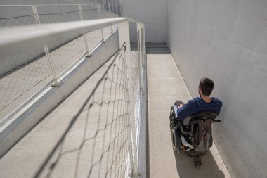 Man on wheelchair, approaching the building moving along an accessible ramp for persons with disability