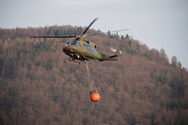 Localized wildfire with the helicopter dropping water by using a water bucket attached to a long line under the helicopter