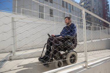 Man on wheelchair, approaching the building moving along an accessible ramp for persons with disability