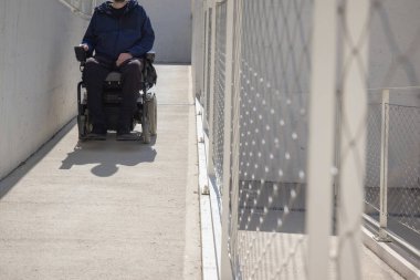 Man on wheelchair, approaching the building moving along an accessible ramp for persons with disability