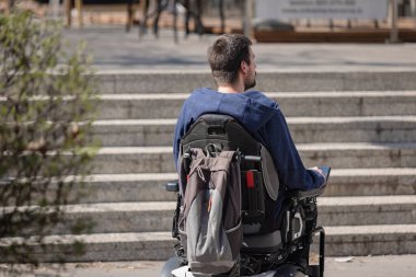 Person with disability on electric wheelchair stopping at the bottom of inaccessible staircase, unable to reach the top
