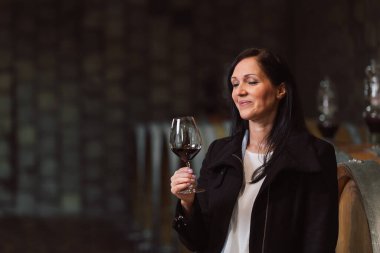 Woman tasting wine at the wine cellar with barrels in background