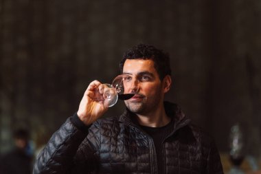 Man in the wine cellar with barrels in background drinking and tasting wine.