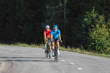 Spor formalı, bisiklet kasklı ve güneş gözlüklü, asfalt yolda pedal çeviren profesyonel yol yarışı çifti.