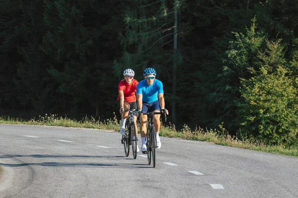 Professional road racing cyclist couple in sports jerseys, wearing bike helmets and sunglasses pedaling on an asphalt road