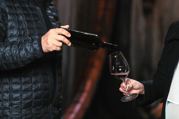 Man pouring fine red wine to a charming woman, in front of a large old wooden barrel in an authentic traditional wine cellar