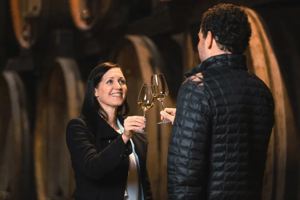 Medium view of the Caucasian couple during a wine tasting in a wine cellar, with large oak barrels in the background