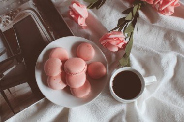 Beyaz arka planda bir fincan kahve ve gül çiçekli pembe makarna kurabiyeleri. Bahar natürmort. Klasik pastel tarzı fotoğraf. Metin için boşluk kopyala. Tonu ayarlanmış resim.