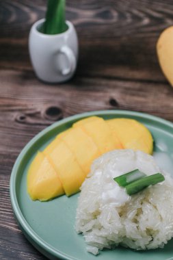 Ahşap masada hindistan cevizi sütüyle servis edilen lezzetli mango yapışkan pilavı. Tayland 'ın popüler geleneksel tatlısı..