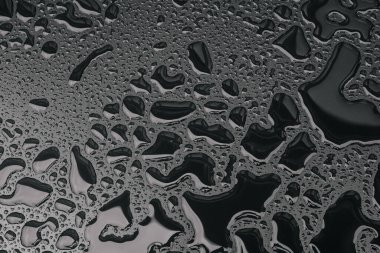 Siyah yüzeye su damlaları düşer. Pencereye konmak için yağmur damlaları, sonbahar havası konsepti,