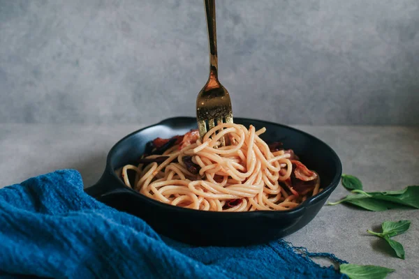 Hand holding fork wrapped on delicious spaghetti with basil, bacon, sauces, green pepper, Hot chili and vegetables.