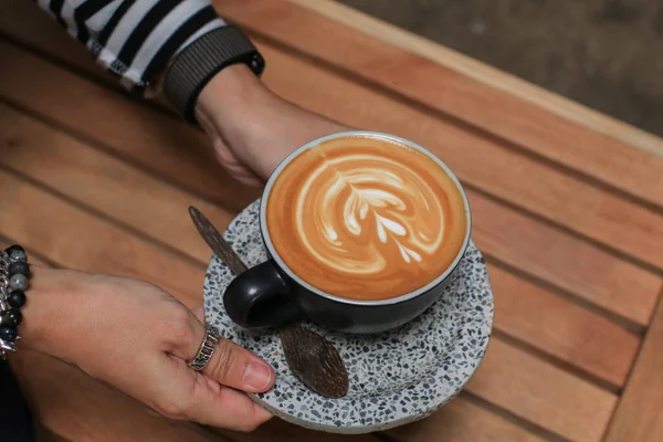 Tangan Memegang Secangkir Kopi Dengan Busa Seni Latte Atas Meja — Stok Foto
