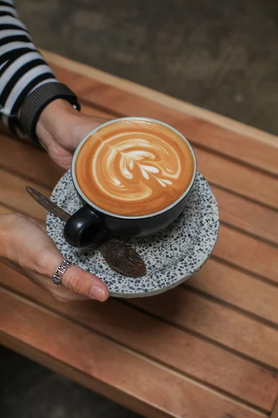 Tangan Memegang Secangkir Kopi Dengan Busa Seni Latte Atas Meja — Stok Foto