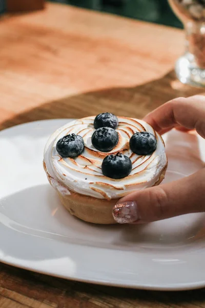 Hand pick up Lemon meringue and blueberry tart in white plate on wooden table. Pie Dessert. Horizontal Copy space