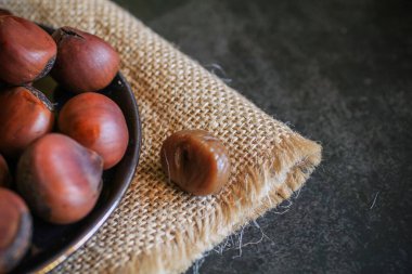 Chestnuts in black bowl over grey background. Pile of fresh chestnuts ready to roast. Top view, copy space.