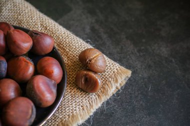 Chestnuts in black bowl over grey background. Pile of fresh chestnuts ready to roast. Top view, copy space.