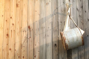 Old rusted metal watering can hanging on the brown wooden wall under sunlight. The concept of gardening. Provence.