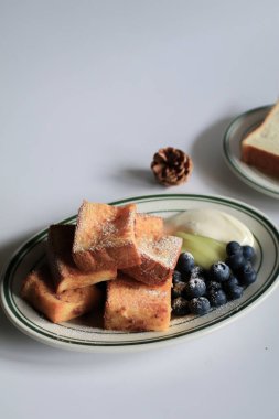 Beyaz tabakta servis edilen yaban mersinli, kivili ve şuruplu ev yapımı Fransız tostu. Sağlıklı bir tatlı konsepti için aşk.