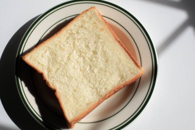 Sabah güneşinin altında beyaz tabakta ev yapımı kaygan ekmek. Kahvaltı ekmeği ve kahve..