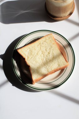 Sabah güneşinin altında beyaz tabakta ev yapımı kaygan ekmek. Kahvaltı ekmeği ve kahve..