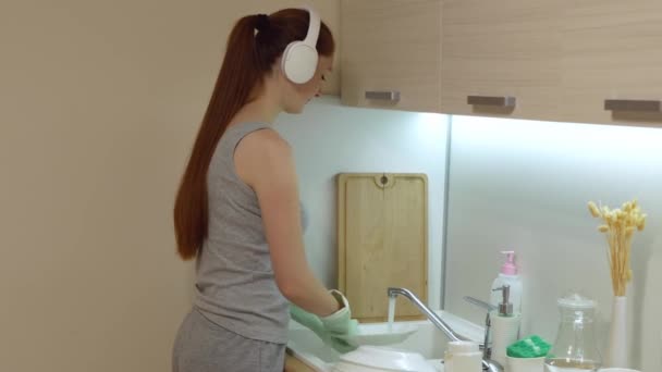 Νεαρή Κοκκινομάλλα Πλένει Πιάτα Και Ακούει Μουσική Στην Κουζίνα Ελκυστική — Αρχείο Βίντεο