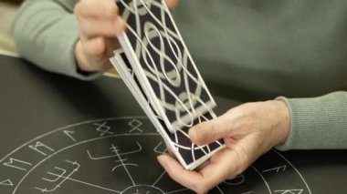 Yetişkin bir kadın tarot kartlarını karıştırıyor. Falcı kadının elleri masada tarot mihrabıyla kart karıştırıyor. Tahmin konsepti.