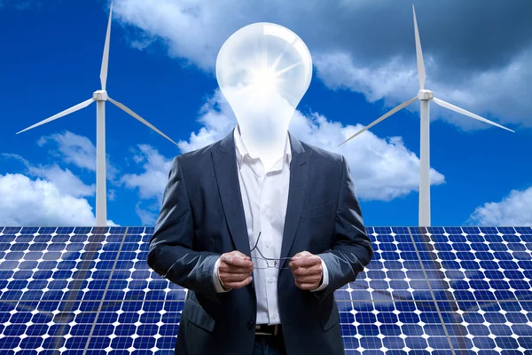Uomo con una testa di lampadina davanti a pannelli solari e turbine eoliche — Foto Stock