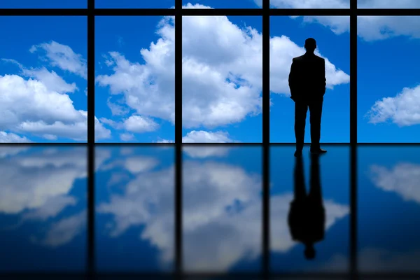 Hombre de negocios mirando por la ventana de oficina de gran altura en el cielo azul y las nubes Fotos de stock libres de derechos