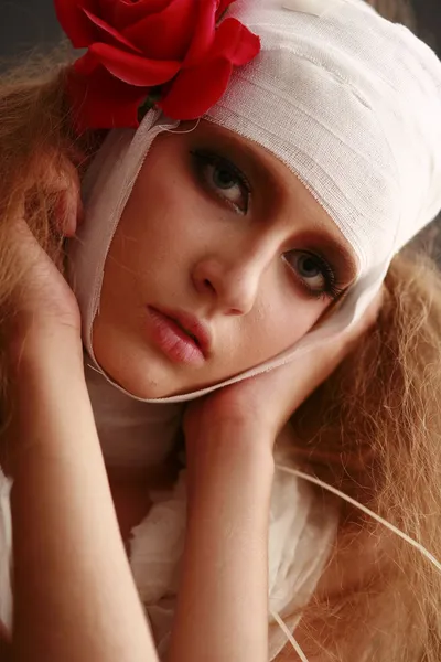 Chica joven y frágil de pie en un albornoz con una cabeza vendada, flor roja enferma en el pelo Fotos de stock libres de derechos